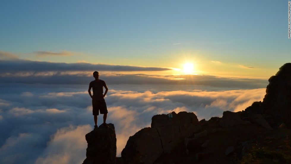 Shadowy figure of man standing on the top of a mountain top overlooking the sunset.